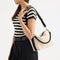 hover | The Daily Crossbody in Black and White Raffia-Knit, carried over the shoulder of a female model, shown from the right.